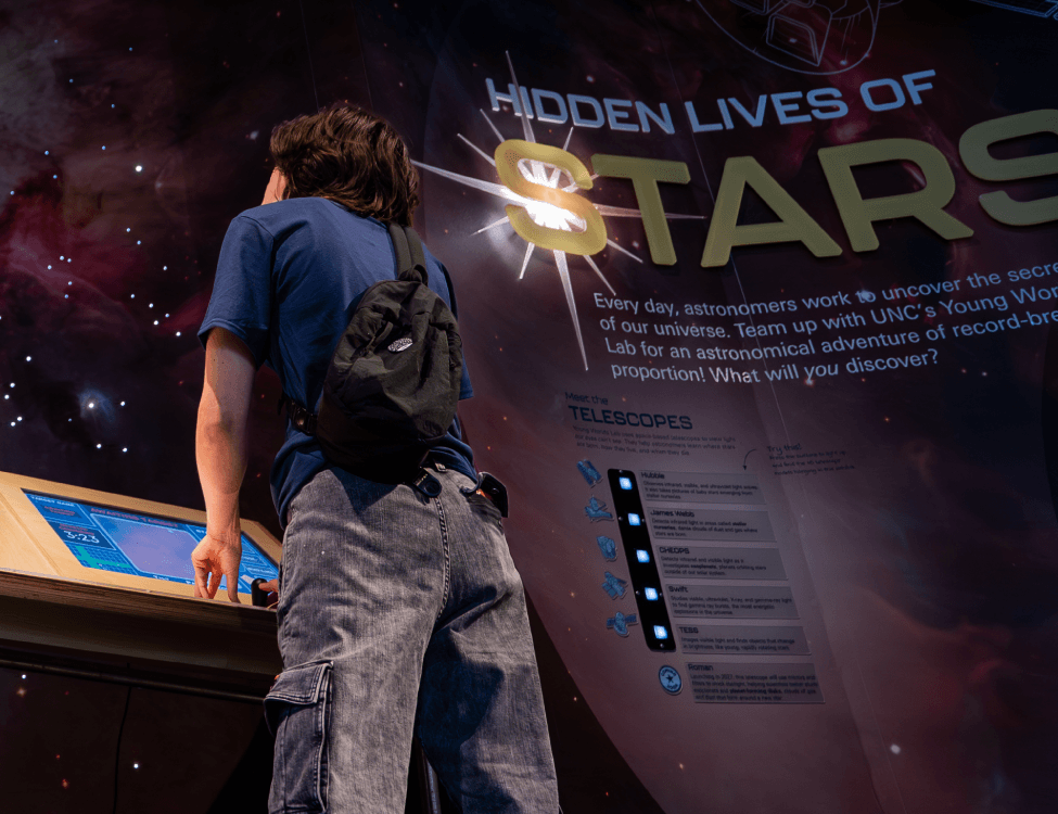 Photograph of a visitor interacting with a kiosk in front of the Hidden Lives of Stars exhibit sign
